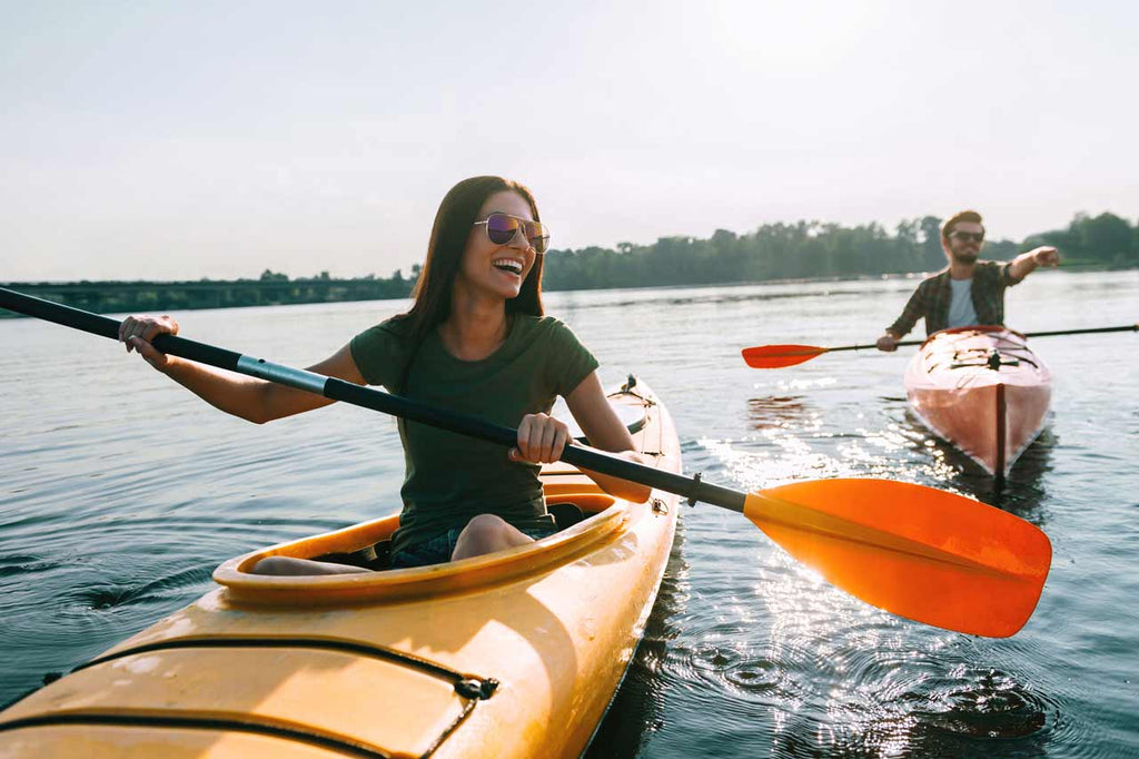 Young smiling couple wearing sunglasses paddles individual kayaks together