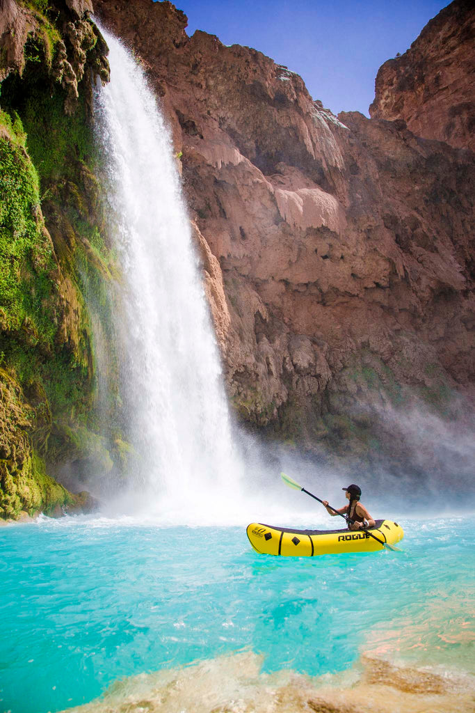 Woman using Rogue-Lite Packraft underneath on water next to a waterfall