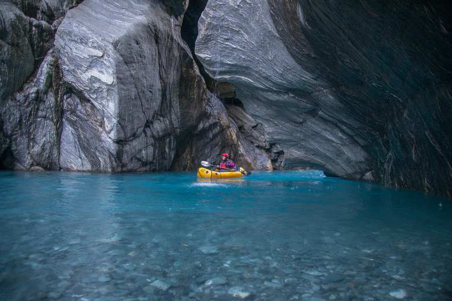 Individual on a Whitewater Packraft navigating the waters surrounded by a cave