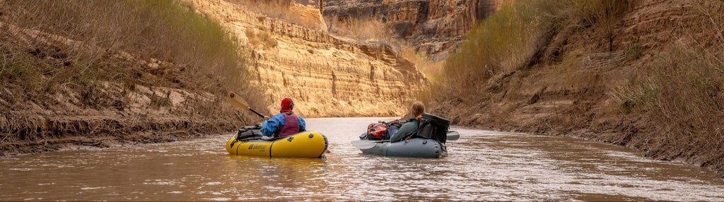 Two people in inflatable rafts navigating a river through a canyon.