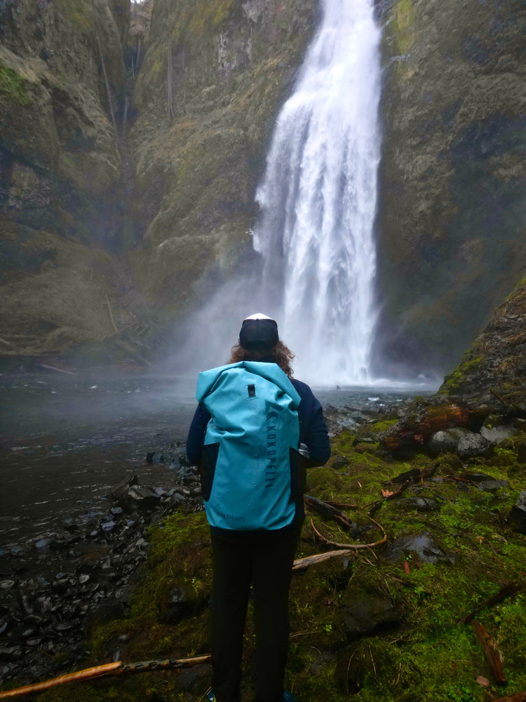 Person facing waterfall while wearing a backpack with a Chasm-Lite Inflatable SUP packed inside it