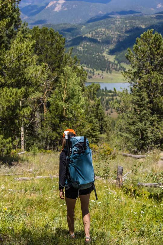 Person walking a forest trail while wearing a backpack with the Chasm-Lite Inflatable SUP packed inside it